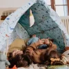 Cabane à construire en bois Pack Libellule avec tissu bleu à motifs nature, enfants allongés dedans
