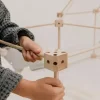Mains d'enfant assemblant une pièce en bois du kit cabane 1001 Cabanes Sarbakane