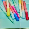 Bougies spirales multicolores en cire posées sur carrelage turquoise et décor floral.