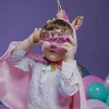 Enfant avec cape rose et serre-tête licorne tenant bouteille sensorielle arc-en-ciel rose.