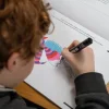 Enfant coloriant un dinosaure rose, rouge et bleu dans le cahier Blink Book.