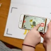 Smartphone scannant un dessin animé de mouton blanc sur cahier Comptines de la ferme.