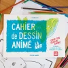 Cahier de dessin animé La mer avec couverture bleue et verte, crayons colorés autour.