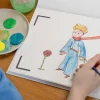 Cahier dessin animé Le Petit Prince avec personnage en bleu et fleur rose peint à l'aquarelle