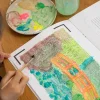 Enfant peignant au pinceau un pont orange sur un cahier Blink Book Monet.