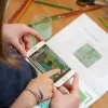 Enfant tenant un smartphone devant cahier de dessin animé Blink Book Monet coloré et crayons autour