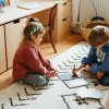 Deux enfants assis sur tapis blanc graphique jouant avec tablette et cartes Kidydraw-mini.