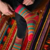 Chaussettes hiver Freja multicolores rayées rouges, jaunes, vertes et bleues, portées sur jeans noirs.