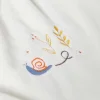 Broderie d’escargot bleu et orange avec feuillage jaune sur tissu blanc du doudou Kaloo.
