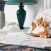 Doudou Renard Léonard orange et blanc en tissu doux assis sur un lit fleuri
