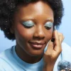 Yeux et ongle avec gel pailleté bleu argenté GalaxSiSi, peau foncée, cheveux bouclés noirs.