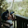 Garçon avec casquette noire utilisant jumelles antichoc Kidybinocular bleu marine en extérieur
