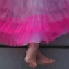 Jupe froufrou Rose Ratatam en tulle à volants, jambes d’enfant croisées, pieds nus.