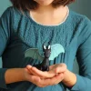 Dragon noir en pâte à modeler avec ailes bleues tenu par enfant en robe bleue