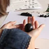 Mains tenant une boule d'argile noire du kit créatif Les dragons, instructions en arrière-plan.