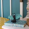 Petit dragon noir aux ailes turquoise posé sur un carnet décoré bleu et vert.