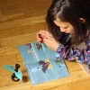 Fille lisant un livret coloré avec un petit dragon noir aux ailes vertes Kit créatif Les dragons.