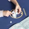 Mains d'enfant décorant un papillon blanc en feutrine avec perles bleues, instructions visibles.