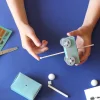 Mains assemblant un véhicule bleu clair avec roues crantées et baguette en bois, kit créatif L'espace.