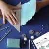 Mains assemblant modèle papier bleu avec roues, pinceaux, et instructions kit créatif l'espace.