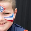 Visage d'enfant avec drapeau français peint en bleu blanc rouge et ballon de foot rouge et bleu sur le front