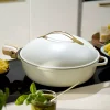 Poêle blanche 28 cm Cookut avec couvercle doré et manche en bois, posée sur plaque noire.