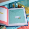 Livre de naissance Puce et Pilou ouvert avec enveloppe bleue à pois blancs et motif planète
