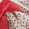 Tissu doux blanc à motifs cœurs rouges avec vêtement en tissu rouge de poupée Emilie Kaloo.
