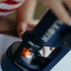 Microscope portable Kidymicroscope bleu avec objet orange sur la platine, main d'enfant visible