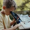 Garçon utilisant un microscope portable Kidymicroscope bleu foncé sur table en bois dehors