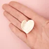 Mini pince à cheveux forme cœur blanc nacré posé dans une main ouverte.
