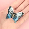 Mini pince à cheveux papillon bleu en plastique transparent avec nervures noires.
