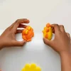 Mains tenant des formes orange et jaune en pâte à modeler lavante l'Optimiste Nailmatic