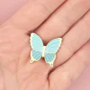 Pin's papillon en métal doré avec ailes bleues claires, posé sur une main.