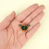 Pin's en émail en forme de papillon noir avec détails orange et blancs, fond doré.