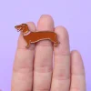 Pin's métal teckel marron avec collier rose sur doigts fond violet.