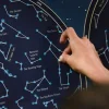 Main plaçant un sticker bleu phosphorescent sur poster noir de constellations Poppik