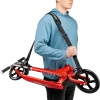 Homme portant une sangle noire BUDDY Puky transportant une trottinette rouge pliée