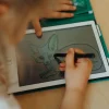 Tablette à dessin Kidydraw-mini verte avec enfant dessinant un fennec sur écran gris.