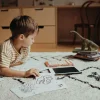 Enfant allongé sur tapis avec tablette à dessin Dinosaure Kidydraw Mini et cartes dinosaures.
