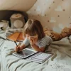 Enfant allongé sur lit, utilisant la tablette à dessin Dinosaure Kidydraw Mini avec stylet noir.