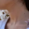 Tatouage éphémère colibri coloré posé sur épaule femme, fond fleurs blanches