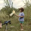 Enfant regardant dans télescope Kidytélescope bleu sur trépied argenté en herbe verte.
