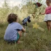 Garçon en short vert utilisant télescope astronomique Kidytélescope bleu sur herbe, fille debout avec décorations célestes en