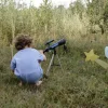 Enfant en t-shirt bleu accroupi regardant dans télescope astronomique Kidytélescope noir et bleu sur herbe.